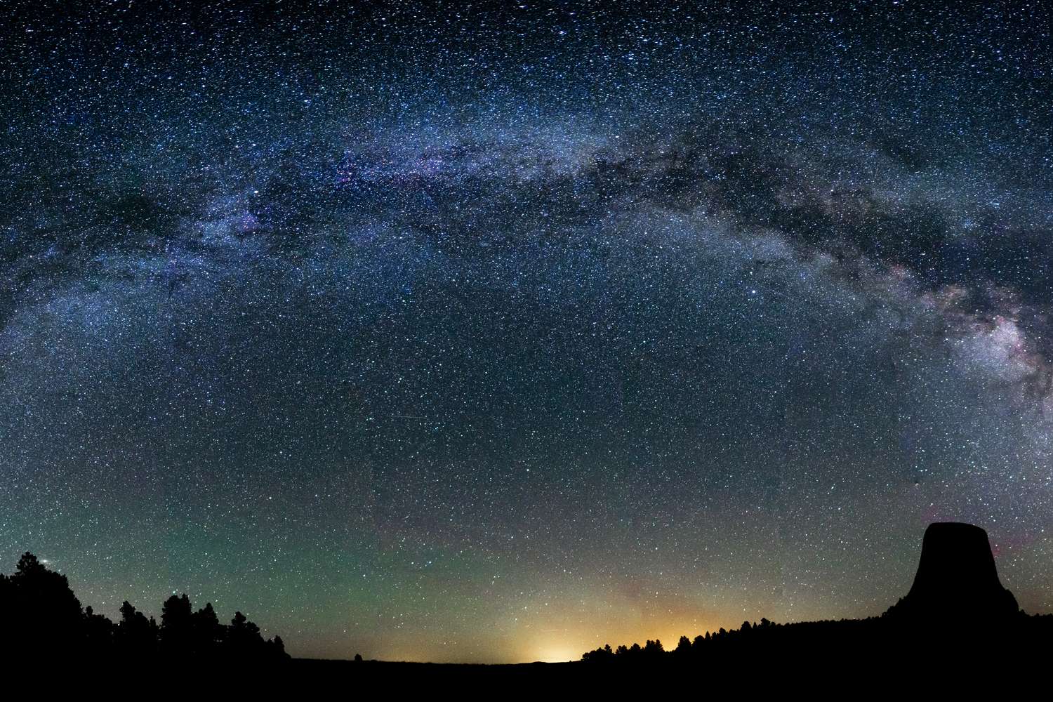 Devils Tower against a night sky full of stars, the Milky Way arching overhead.
